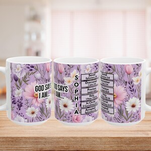 May include: Three white ceramic mugs featuring a light purple background with a floral pattern of pink and white flowers. The text reads GOD SAYS I AM, the name SOPHIA, and a list of biblical affirmations including Saved, Overcomer, and Accepted.