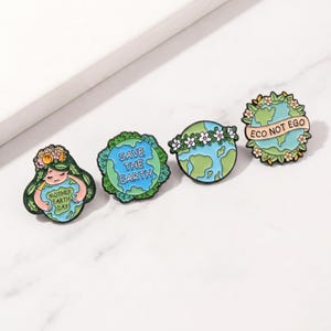 May include: Four enamel pins with environmental themes. One pin features a woman with floral hair holding a heart that says "Mother Earth Day." Other pins show the Earth with the phrases "Save the Earth" and "Eco Not Ego."