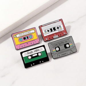 Puede incluir: Cuatro pines de esmalte con forma de cintas de cassette retro. Los pines son de color rosa, rojo, verde y gris. El pin rosa dice "Best of the 90's". El pin verde dice "Good Vibes". El pin gris dice "Sad Songs".