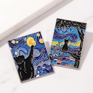 May include: Two rectangular enamel pins featuring a black cat design against a starry night sky, inspired by Van Gogh's artwork. One pin shows a cat reaching for the moon, the other shows a cat perched on a tree branch. The pins have a silver border.