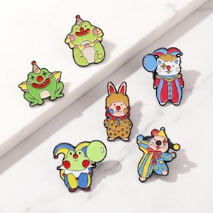 May include: A collection of colorful, cartoonish clown-themed pins. The pins feature various characters, including frogs, a cat, a rabbit, and a mouse, all dressed in clown attire. Each pin has a unique design with bright colors and playful details.
