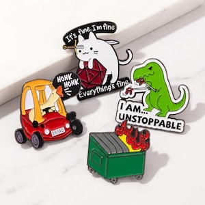 Könnte beinhalten: Set aus vier Emaille-Anstecknadeln mit humorvollen Designs. Enthält eine weiße Katze mit Schwert, einen grünen Dinosaurier, eine Ente in einem roten Auto und ein brennendes Müllcontainer. Jede Nadel hat einen einzigartigen Satz.