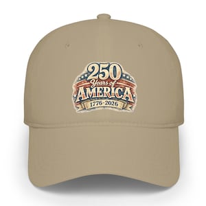 Puede incluir: Gorra de béisbol beige con un diseño patriótico. La gorra presenta un emblema desgastado con el texto "250 Years of America 1776-2026" en rojo, blanco y azul. El sombrero es un diseño clásico de seis paneles con visera curva.