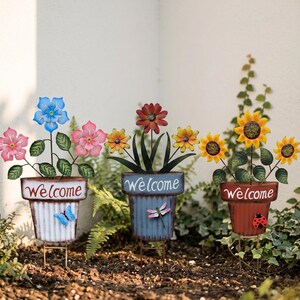 May include: Three metal garden stakes shaped like flower pots, each with a "Welcome" sign. The pots hold colorful metal flowers, including pink, blue, yellow, and red blooms. A butterfly, dragonfly, and ladybug are attached to the pots.