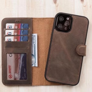 Może przedstawiać: Brązowe skórzane etui na telefon z portfelowym designem. Etui posiada przegródki na karty i kieszeń na gotówkę. Etui na telefon jest otwarte, odsłaniając wnętrze i telefon. Etui wykonane jest z postarzałego materiału skórzanego.