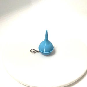 May include: A light blue, 3D-printed funnel-shaped charm with a small silver-coloured clasp. The charm is on a white surface. The funnel has a rounded base and a long, thin spout.