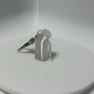 Peut inclure: Un petit porte-clés argenté en forme de pichet. Le charm a une anse et un bec, et est attaché à un porte-clés argenté. Le charm est posé sur une surface blanche.