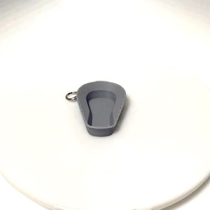 May include: A small, grey, 3D-printed ashtray with a rounded rectangular shape and a key ring attachment. The ashtray has a textured interior and is set against a white background.