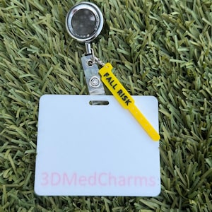 May include: A silver retractable badge reel with a clear plastic strap attached to a white rectangular ID holder. The holder features the pink text 3DMedCharms and a yellow charm shaped like a medical wristband with the black text FALL RISK.