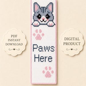May include: A cross-stitch bookmark featuring a gray cat with pink paws and a pink border. The text "Paws Here" is below the cat, with paw prints. The words "PDF Instant Download" and "Digital Product" are on the sides.