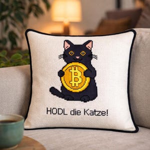 May include: A square cushion with a white background and a black border. It features a cross-stitch design of a black cat holding a gold Bitcoin coin. The text "HODL die Katze!" is stitched below the cat.