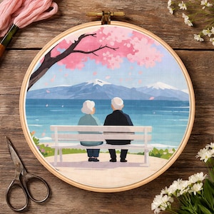 May include: Embroidery hoop featuring a serene scene of an elderly couple sitting on a bench, overlooking a lake and mountains under a cherry blossom tree. The artwork is in soft pastel colors.