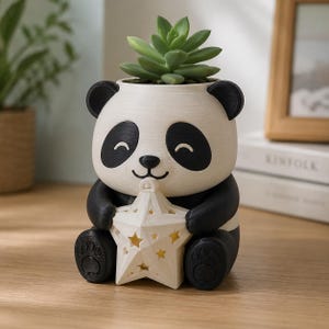 May include: A panda-shaped planter with a textured off-white and black finish, featuring a smiling face and black ears. The panda holds a white, star-shaped object with cut-out star patterns. A green succulent plant is potted inside the top.