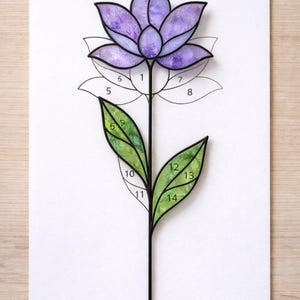 Puede incluir: Un diseño de flor de vidriera con una flor morada y hojas verdes. La flor tiene un contorno negro y está numerada para facilitar el montaje. El diseño está sobre un fondo blanco.