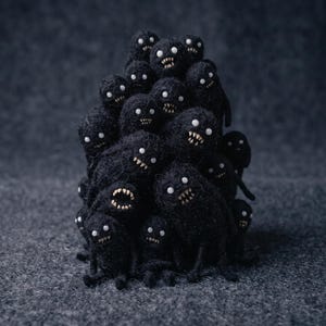 May include: A cluster of small, black, fuzzy creatures stacked together. Each creature has a round body, two white circular eyes, and a wide mouth filled with small, pointed white teeth. The texture of the figures appears soft and fibrous.