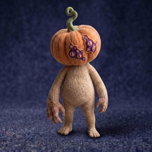 Könnte beinhalten: Eine stehende Figur mit einem strukturierten beigen humanoiden Körper und einem großen orangefarbenen Kürbiskopf. Der Kürbis hat einen grünen Stiel und zwei violette Flecken, die jeweils mehrere gelbe Augen mit dunklen Pupillen enthalten.