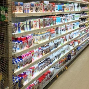 May include: A grocery store aisle filled with various food products. Shelves are stocked with boxes, bottles, and containers of different brands and types of food items. The products include breakfast cereals, protein shakes, and other packaged goods.