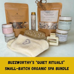 May include: A collection of spa products, including jars of sugar scrub, bath salts, a body brush, and a pair of socks with a heart design. The products are arranged on a light blue surface. The text "BUZZWORTHY'S 'QUIET RITUALS' SMALL-BATCH ORGANIC SPA BUNDLE" is at the bottom.