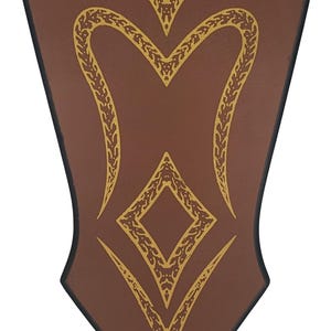 Könnte beinhalten: Braunes schildförmiges Dekorationsstück mit goldfarbenen, verzierten Designs. Das Schild hat einen schwarzen Rand und weist eine rautenförmige Form und geschwungene Linien auf. Das Design ist symmetrisch und detailliert.