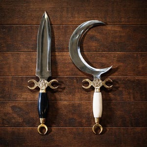 May include: Two decorative metal blades with crescent moon and dagger designs. The dagger has a black handle, while the other has a white handle. Both have gold-colored accents and a star emblem.