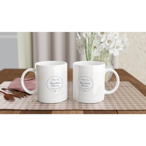May include: Two white ceramic mugs featuring a circular logo with the text I Pick Up Random Pieces on the Beach. Each mug has a standard handle and a smooth finish. The design is centered on the front of each mug, displaying clear black text.