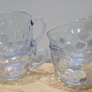 Puede incluir: Un juego de cuatro tazas de cristal transparente con un patrón de burbujas circulares en relieve en el exterior. Cada taza tiene un asa curva y un borde ancho, mostrando un diseño transparente que refleja la luz sobre la superficie.