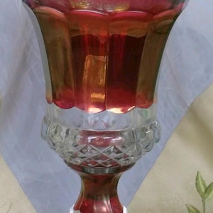 May include: A decorative glass vase with a lid. The vase has a clear, diamond-cut base and stem, transitioning to a red and gold-colored body. The lid is also clear with a diamond-cut pattern.