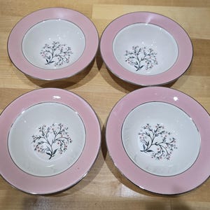May include: Four matching pink and white bowls with a floral design. The bowls have a pink rim with a silver edge and a white interior. The floral design features a black stem with small pink and white flowers.