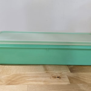 May include: A light green plastic storage container with a clear lid. The container is rectangular and has a smooth surface.