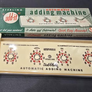 Könnte beinhalten: Vintage Sterling "add-it" automatische Rechenmaschine in der Originalverpackung. Die cremefarbene Maschine hat vier Zifferblätter mit roten und weißen Zahlen. Die Box ist grün und weiß mit dem Text "Automatic Adding Machine".
