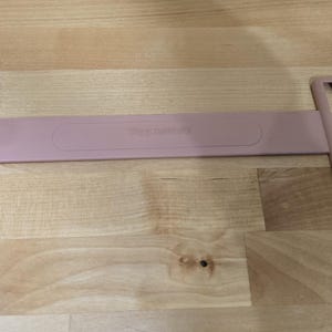 May include: A pink plastic cable organiser with two rectangular openings and the word "remarkable" printed on the connecting strap.