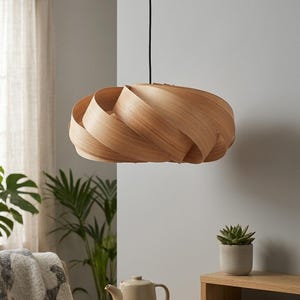 Puede incluir: Una lámpara colgante de madera de color marrón claro con un diseño en espiral. Cuelga de un cable negro. La habitación tiene paredes neutras y una mesa auxiliar de madera con una planta suculenta y libros. El diámetro de la lámpara es de unos 40 cm.