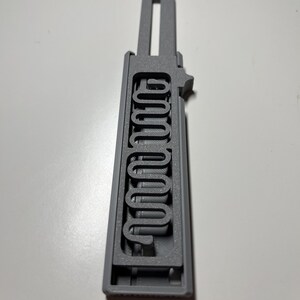 May include: A gray 3D-printed key-shaped object with the word "200000" printed vertically. The key has a rectangular body with a series of curved lines forming the numbers. The top has a rectangular hole.