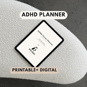 Puede incluir: Un planificador digital ADHD Focus en una tableta, con el texto "ADHD Planner" y "Printable + Digital". El planificador presenta un logotipo de pingüino y se muestra sobre una superficie blanca texturizada.