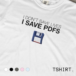 Könnte beinhalten: Ein weißes T-Shirt mit dem schwarzen Text "I DON'T SAVE LIVES I SAVE PDFS" über einer Grafik einer blauen Diskette. Das T-Shirt hat einen Rundhalsausschnitt und ein sichtbares Etikett am Kragen. Fünf kleine farbige Kreise sind unten zu sehen.