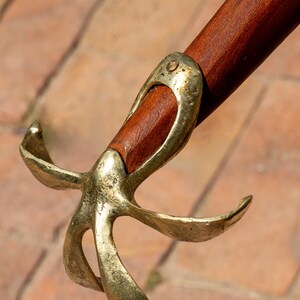 May include: Close-up of a sword hilt. The hilt features a dark wooden grip and a brass guard with a stylized, four-lobed design. The brass has a slightly aged appearance.