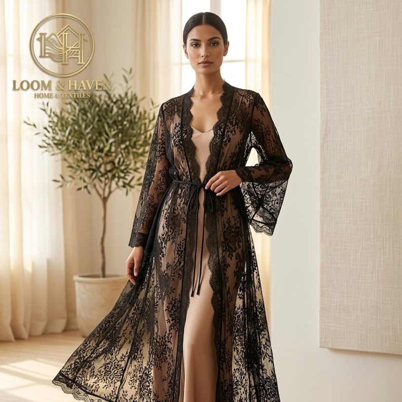 May include: A floor-length black lace robe featuring intricate floral patterns, long flared sleeves, and a thin black tie closure at the waist. The robe is worn over a solid beige slip dress. The Loom & Haven Home & Textiles logo is visible.