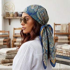 May include: A blue paisley patterned silk scarf tied at the back of the head. The scarf features a mix of blue, gold, and white colors. The scarf is worn with sunglasses and a white shirt. The logo "LOOM & HAVEN HOME & TEXTILES" is visible in the background.
