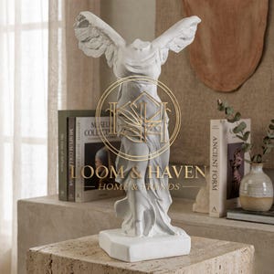 Puede incluir: Estatua blanca de Niké, la diosa griega de la victoria, sin cabeza, con las alas extendidas. La estatua está sobre una base blanca y se exhibe sobre una superficie de piedra. La imagen incluye el texto "LOOM & HAVEN HOME & TRENDS".