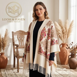 May include: Cream-colored shawl with a paisley pattern in pink, red, and brown. The shawl has a fringed edge and is draped over a black outfit. The image includes the text "LOOM & HAVEN HOME & TEXTILES".