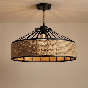 May include: A rustic ceiling light fixture with a black metal frame and a woven rope shade. The light hangs from a rope and has a single exposed bulb. The fixture has a circular design and is suitable for indoor lighting.