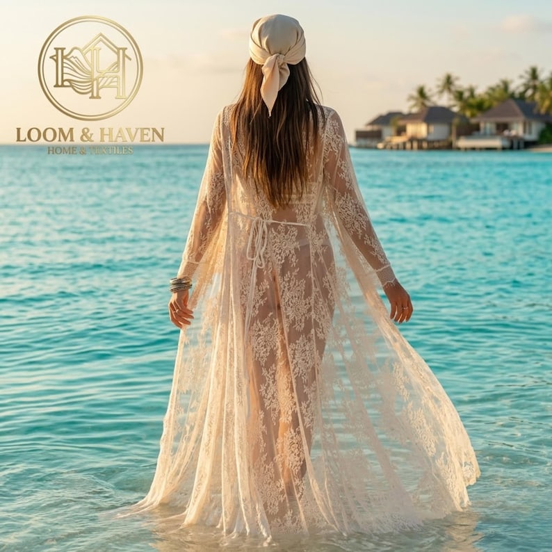May include: A floor-length, sheer beige lace cover-up featuring long sleeves, a tie-waist closure, and intricate floral patterns. The garment is worn with a matching beige headscarf, showcasing a delicate, semi-transparent design.