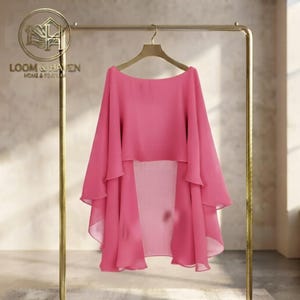 May include: A bright pink, lightweight, semi-sheer cape-style top featuring a wide, boat-neck design and flowing, layered fabric panels that drape down from the shoulders. The garment is displayed on a gold-toned metal hanger.