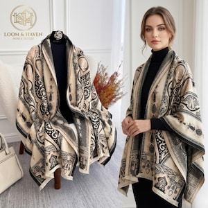 May include: A beige and black patterned shawl with a decorative design. The shawl is draped over a mannequin and worn by a person. The shawl has a black border and is made of a soft material. The logo "LOOM & HAVEN HOME & TEXTILES" is in the top left corner.