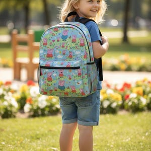 Puede incluir: Una mochila azul claro con un estampado repetido de un personaje de cerdito de dibujos animados, flores y nubes. La mochila tiene correas negras, un bolsillo frontal y bolsillos laterales de malla. El niño lleva una camiseta azul, pantalones cortos vaqueros y zapatillas blancas.