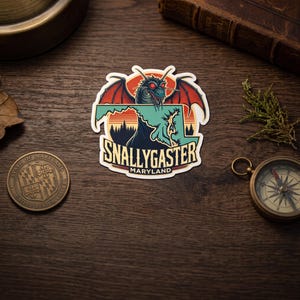 May include: A die-cut sticker featuring a mythical Snallygaster creature with red eyes and wings, positioned over a light green map of Maryland. The design includes a sunset, a dark forest silhouette, and the text SNALLYGASTER MARYLAND in bold.
