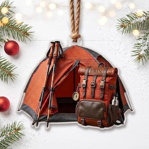 May include: A hanging ornament shaped like an orange tent with two trekking poles and a brown backpack featuring the name ERIN, a small compass charm, and a silver water bottle attached to the side, suspended by a thick tan rope.