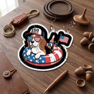 May include: A die-cut sticker featuring a cartoon beagle wearing sunglasses with an American flag pattern and a cap labeled 250 AMERICA. The dog sits in a red, white, and blue inner tube with a bottle and a small American flag attached to the side.