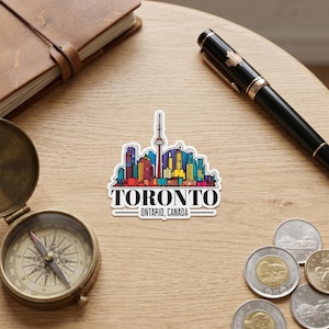 May include: A die-cut sticker featuring a colorful illustration of the Toronto skyline, including the CN Tower, with the text TORONTO ONTARIO, CANADA printed in black capital letters at the bottom of the design.
