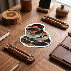 May include: A sticker featuring a stack of vinyl records in various colors including black, orange, and light blue, with a small orange record player integrated into the pile. The illustration has a white border and a flat, graphic design style.